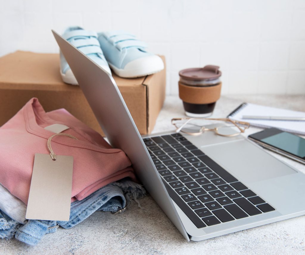 Notebook e roupas próximas de uma caixa de papelão para simbolizar um e-commerce de roupas