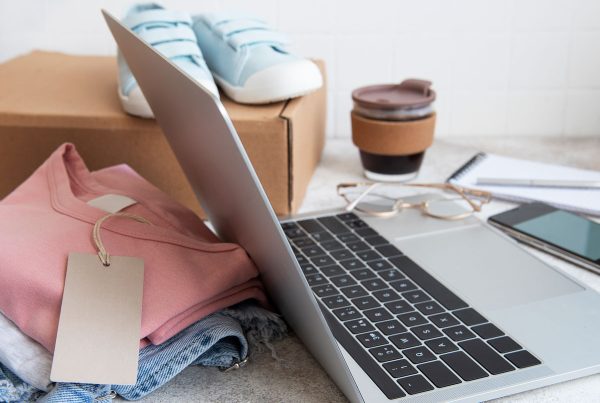 Notebook e roupas próximas de uma caixa de papelão para simbolizar um e-commerce de roupas