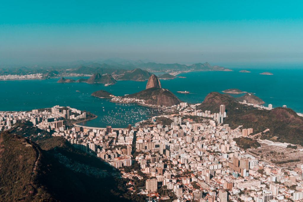 Visão de cima da cidade do rio de janeiro onde é possível ver a lagoa, a bahia de guanabara, vários prédios e o pão de açúcar