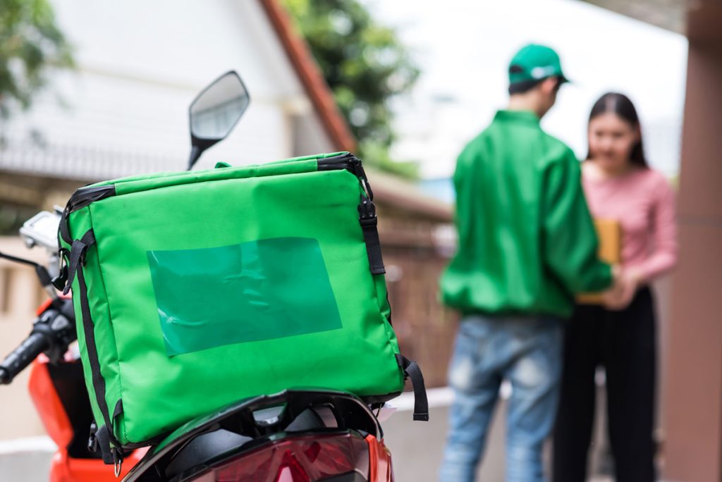 uma mulher recebendo o produto comprado por ela de um entregador homem em uma moto